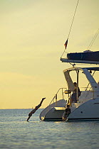 Woman diving off the stern of a cruising catamaran. Model and Property Released.