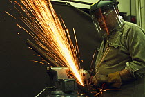 Boat builder grinding metal in a shipyard's metal workshop.