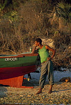 A local man leaning on his fishing boat on a stony beach, Cuba.