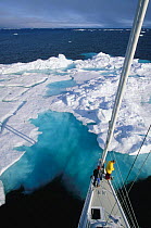 Mast view of the crew of 88ft sloop superyacht "Shaman" watching from the bow as the yacht approaches a large iceberg, Spitsbergen, Svalbard, Norway.