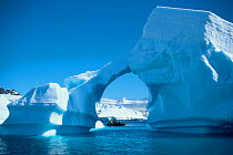 An expedition group in a RIB under a natural archway in an iceberg, Antarctic Peninsula.