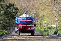 Red jeep towing a yacht on a trailer.