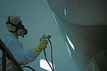 Spray painting the hull of a boat in a spray painting booth, Hinckley, Rhode Island, USA.