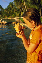 Young girl holding a conch shell on beach, Belize.