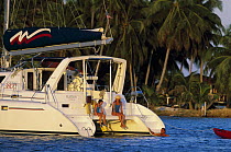 Two people sitting on the back of a cruising catamaran with a man in the water, Belize.