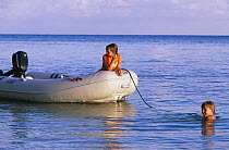 Boy swimming from an inflatable tender with another in the boat, Belize.