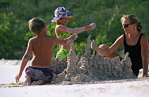 A mother and her children building sand sculptures on the beach. Model released.