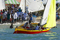 Locals sailing a traditional boat with a crowd watching from the shore, Grenada Sailing Festival 2005, Grenada, Caribbean.