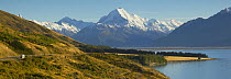 Campervan travelling along a lakeside road with snowcapped mountains beyond, South Island, New Zealand.