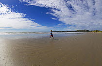 Child running along a long sandy beach, South Island, New Zealand.