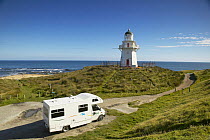 Camper van driving towards a lighthouse on the coast, South Island, New Zealand.