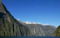Yacht in distance, cruising through steep fiords of fiordland, South Island, New Zealand.