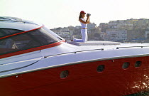 Woman filming from the foredeck of high performance motoryacht "Azzurra 63'", as it cruises off Procida Island, Italy. The luxury yacht was built by Naples-based specialist Cantieri di Baia. It is 18....