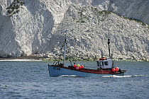 A fishing boat cruising alongside the white cliffs that lead to The Needles, Isle of Wight, England, UK.