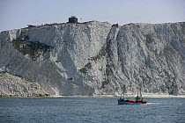 A fishing boat cruising alongside the white cliffs that lead to The Needles, Isle of Wight, England, UK. The Needles Old Battery can be seen on top of the cliff, as can the look out post (far left), r...