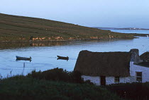 Thatched cottage and open boats moored in bay. Sky Road, Connemara, Ireland.