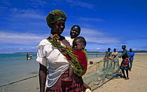 Mother and baby on the beach with local fishermen pulling in nets behind, Benguerra Island, Mozambique