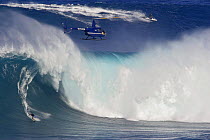 Helicopter filming tow-in surfer at Peahi (Jaws) off Maui, Hawaii, with jetskier pulling another surfer into the next wave in the top of the frame.