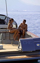 Couple sitting on bar stools on the deck of a power boat, with the transom doors open. Motorboat "One", Cantieri di Baia, off the coast of Baia, Naples, Italy.