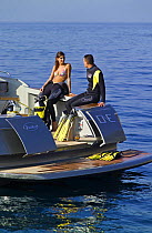 Couple in wetsuits ready to go scuba diving from a power boat, with the transom doors open. Motorboat "One", Cantieri di Baia, off the coast of Baia, Naples, Italy.