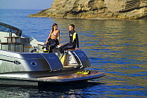 Couple in wetsuits ready to go scuba diving from a power boat, with the transom doors open. Motorboat "One", Cantieri di Baia, off the coast of Baia, Naples, Italy.