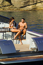Couple sitting on bar stools the deck of a power boat, with the transom doors open. Motorboat "One", Cantieri di Baia, off the coast of Baia, Naples, Italy.