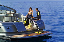 Couple in wetsuits ready to go scuba diving from the stern of a power boat, with the transom doors open. Motorboat "One", Cantieri di Baia, off the coast of Baia, Naples, Italy.