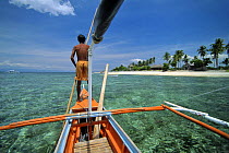 Man standing on the bow of his Banca, a typical fishing boat in the Philippines, near the coast of Balicasag Island (Bohol), Philippines.