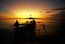 Local outrigger boat sails into the sunset. Balicasag Island, Bohol, Philippines.