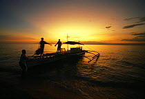 Local outrigger boat unloading on the beach at sunset. Balicasag Island, Bohol, Philippines.