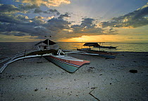 Local banca fishing boats pulled up on the coral beach of a small island at sunset. Balicasag Island, Bohol, Philippines.