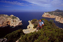 Trekker on highest point of Capo Caccia, with a view of the archipelago and Fordedada island. Sardinia, Italy.