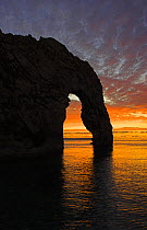Sun setting through the arch at Durdle Door, Jurassic Coast World Heritage Site, Dorset. November.