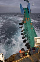 Crewmen working on a fishing net as the rubber rock hopper discs are lowered over the stern ready to be cast into the sea, August 2006.