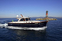 Portland 55 motoryacht, built by Abati yachts, cruising past a lighthouse in the Mediterranean. Tuscany, Italy.