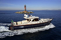 Portland 55 motoryacht, built by Abati yachts, cruising past a lighthouse in the Mediterranean. Tuscany, Italy.