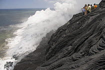 Tourists looking at a lava flow pouring into the Pacific Ocean, Volcanoes National Park, Big Island, Hawaii.
