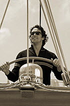 A crew member steering at the helm of a yacht, Calagalera Marina, Grosseto, Italy.
