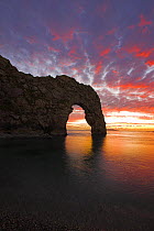 Sun setting through arch at Durdle Door, Jurassic Coast World Heritage Site, Dorset. November.