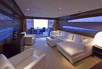 White upholstered interior of Velvet 83', a luxurious motoryacht model from boatbuilders Cantieri Tecnomar, Viareggio, Italy. Patio doors open onto a sun deck with seating.