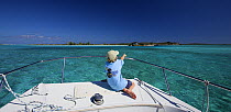 Young boy sitting pointing on deck of Shannon Shoalsailor, this innovative beachboat is a shallow draft boat designed to roam shallow waters such as these, Exuma, Bahamas.
