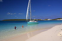 Shannon Shoalsailor moored alongside a sandy beach with children playing in the water. This innovative beachboat is a shallow draft boat designed to roam shallow waters such as these in Exuma, the Bah...