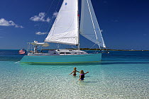 Shannon Shoalsailor moored with two children wading out to it. This innovative beachboat is a shallow draft boat designed to roam shallow waters such as these in Exuma, the Bahamas.