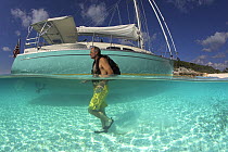 Split-level view of the hull of the Shannon Shoalsailor and a man walking past, illustrating how this innovative, keelless, shallow draft beachboat is designed to roam shallow waters, Exuma, Bahamas.