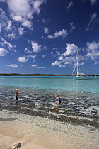 Children playing on the shoreline of a beach with a Shannon Shoalsailor moored beyond. This innovative beachboat is a shallow draft boat designed to roam shallow waters such as these in Exuma, the Bah...