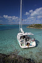 Man putting on fins on board a Shannon Shoalsailor moored in a sandy bay. This innovative beachboat is a shallow draft boat designed to roam shallow waters such as these in Exuma, the Bahamas.