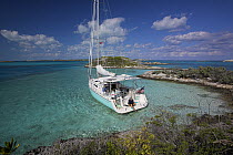 Man putting on fins on board a Shannon Shoalsailor moored in a sandy bay. This innovative beachboat is a shallow draft boat designed to roam shallow waters such as these in Exuma, the Bahamas.