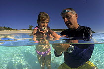 Father and daughter examining shells they have collected from the shallow waters of Exuma, Bahamas.