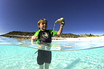 Young boy playing with a shell in the shallow waters of Exuma, Bahamas.