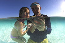 Father and daughter examining a piece of coral in the clear waters of Exuma, Bahamas.